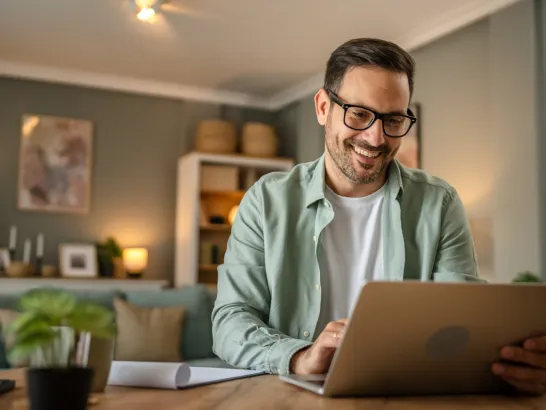 Mann sitzt im Wohnzimmer vor dem Laptop und lächelt