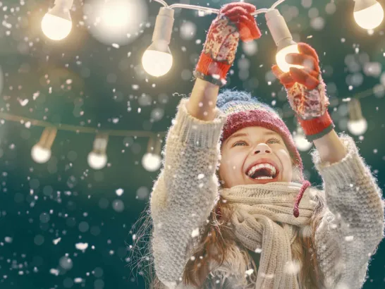 Ein Mädchen mit einer Lichterkette im Schnee.