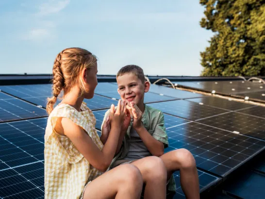 Zwei Kinder sitzen an einer Photovoltaikanalge und lachen sich an.