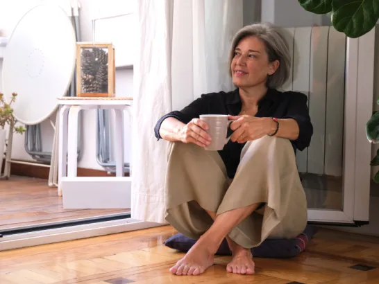 Eine Frau sitzt entspannt mit dem Rücken an einer Heizung und schaut nach draußen.