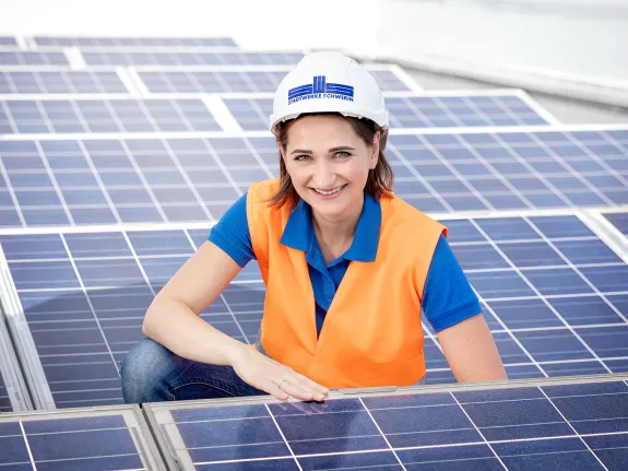 Junge Frau mit Warnweste und Helm kniet zwischen Solarmodulen
