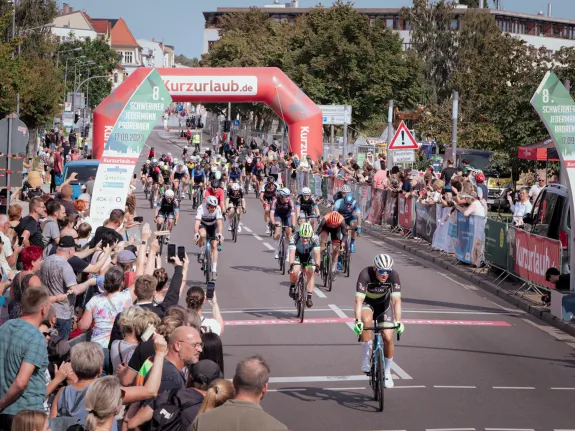 Eine große Gruppe von Sportfahrradfahrern auf der Rennstrecke gesäumt mit Zuschauern.