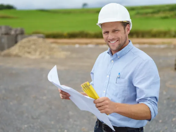 Bauarbeiter mit Bauplan in der Hand lächelt in die Kamera