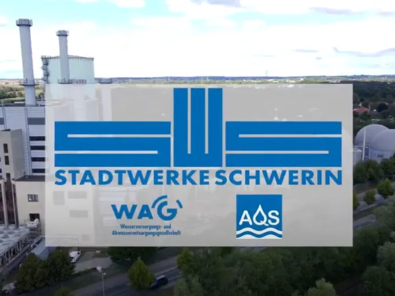 Logo Stadtwerke Schwerin, WAG Schwerin und AQS Schwerin, vor einer Luftaufnahme des Heizkraftwerkes Schwerin Süd