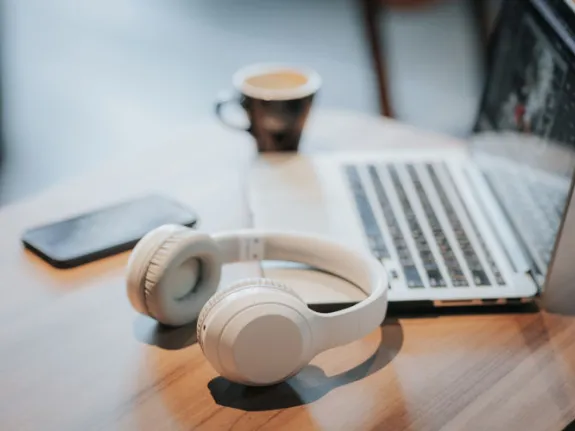 Tisch mit aufgeklapptem Laptop, Handy, Kopfhörern und Kaffeetasse