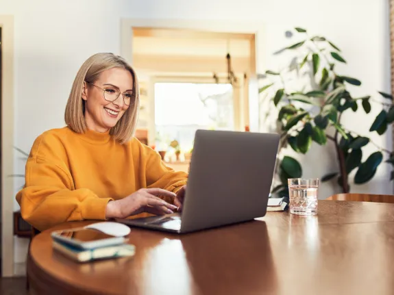 Frau sitzt zuhause am Tisch mit Laptop
