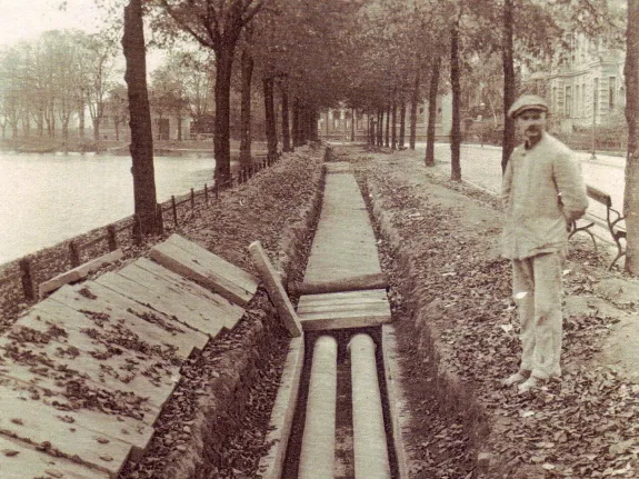 Schwarz-Weiß-Foto der August-Bebel-Straße. Der Fußgängerweg ist aufgegraben. Daneben steht ein Arbeiter.