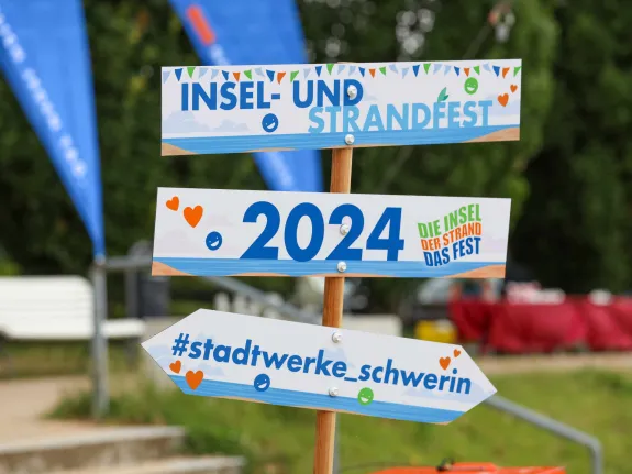 Wegweiser mit drei Hinweisschildern "Insel- und Strandfest", "2024" und "#stadtwerke_schwerin"