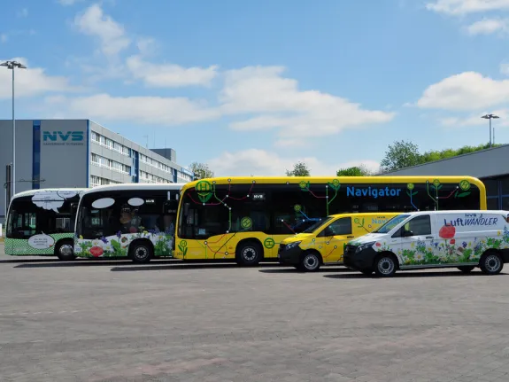 Drei E-Linienbusse mit unterschiedlichen Designs sowie zwei elektrische Transporter stehen vor dem Hauptgebäude des NVS.