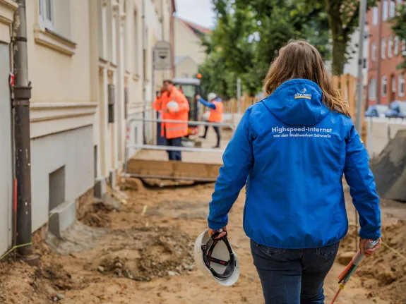 Eine Frau in blauer Arbeitsjacke läuft über eine Baustelle.