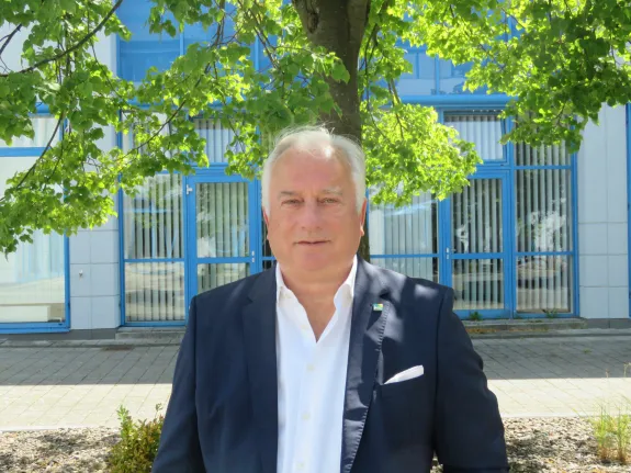 Der Geschäftsführer der Stadtwerke Schwerin Dr. Josef Wolf steht unter einem Laubbaum vor dem Stadtwerkehauptgebäude.