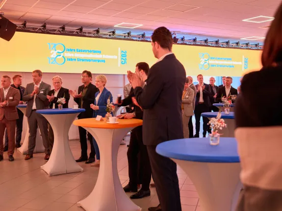 Eine Gruppe von Menschen steht in einem festlich beleuchtetem Raum und applaudiert.
