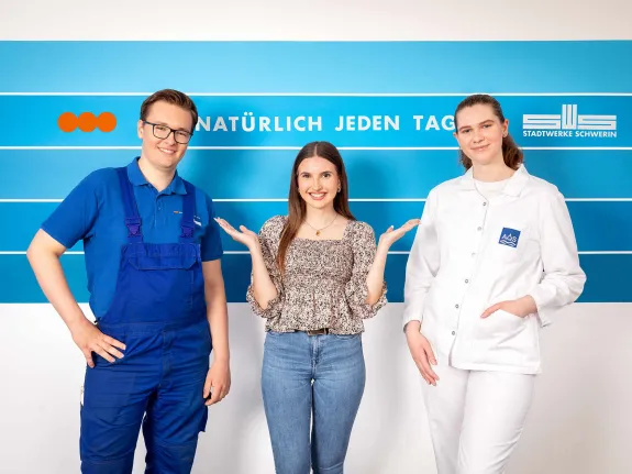 Drei junge Menschen in Berufsbekleidung stehen gut gelaunt beisammen.