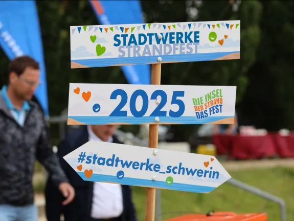 Wegweiser mit drei Hinweisschildern: Stadtwerke-Strandfest , 2025, #stadtwerke_schwerin