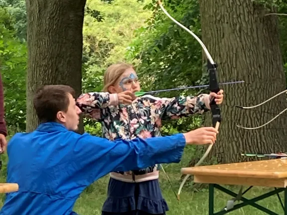 Ein Mädchen spannt einen Bogen und wird von meinem Herren unterwiesen.