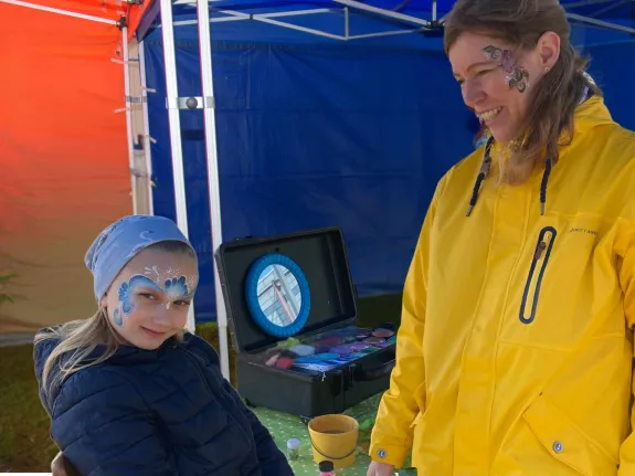 Geschminktes Mädchen lächelt neben Künstlerin in die Kamera.