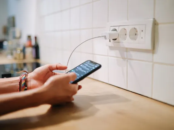 Person tippt auf einem Handy. Das Handy ist an eine Steckdose angeschlossen.