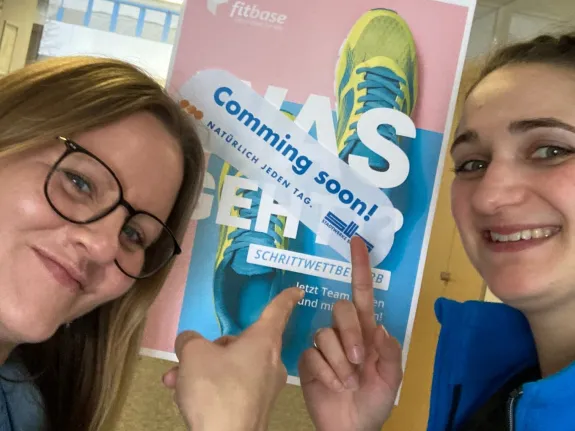 Zwei Frauen stehen vor einem Plakat zum Schrittwettbewerb.