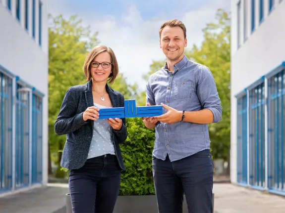 Eine junge Frau und ein junger Mann halten zusammen das blaue Logo der Stadtwerke Schwerin