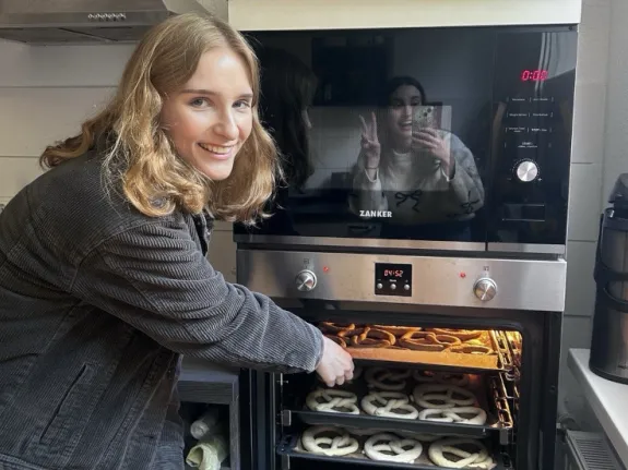 Eine junge Frau steht an einem Backofen und holt Brezel heraus