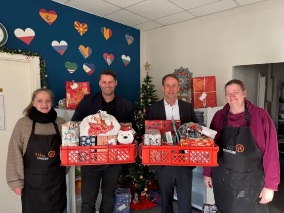 Zwei Männer und zwei Frauen stehen mit Geschenken vor einem Tannenbaum