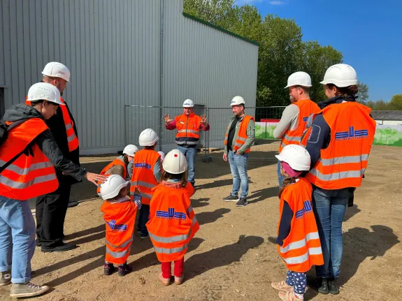 Gruppen mit Erwachsenen und Kleinkindern nehmen mit Warnwesten und Bauhelmen an einer Führung teil