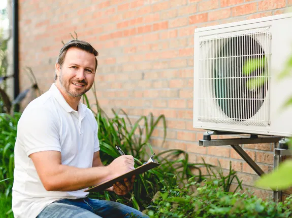 Mann hockt vor Wärmepumpe und notiert etwas