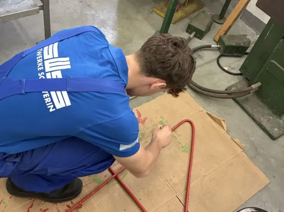 Ein gewerblicher Azubi lackiert eine Metallstange rot