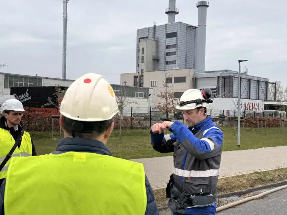 Ein Stadtwerkemitarbeiter mit typischer Arbeitsbekleidung erklärt Besuchenden etwas.