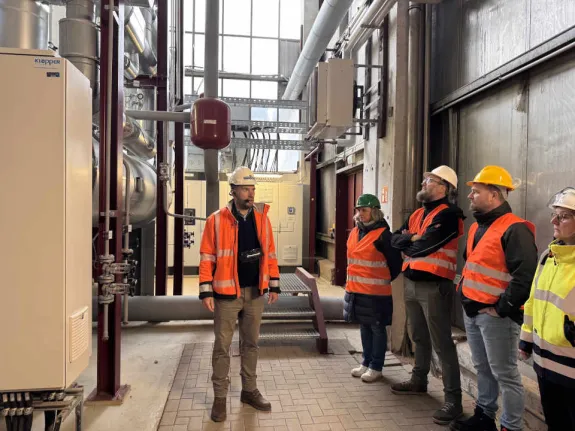 Ein Stadtwerkemitarbeiter mit typischer Arbeitsbekleidung steht im Heizkraftwerk und gibt Auskunft bei einer Führung.
