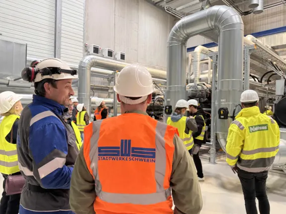 Ein Stadtwerkemitarbeiter mit typischer Arbeitsbekleidung steht vor Hochleistungswärmepumpen und gibt Auskunft zur Funktionsweise bei einer Führung.