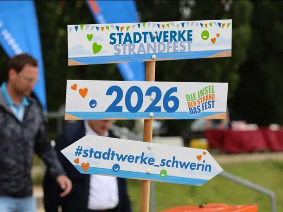 bunter Wegweiser mit drei Hinweisschildern: Stadtwerke-Strandfest , 2026, #stadtwerke_schwerin