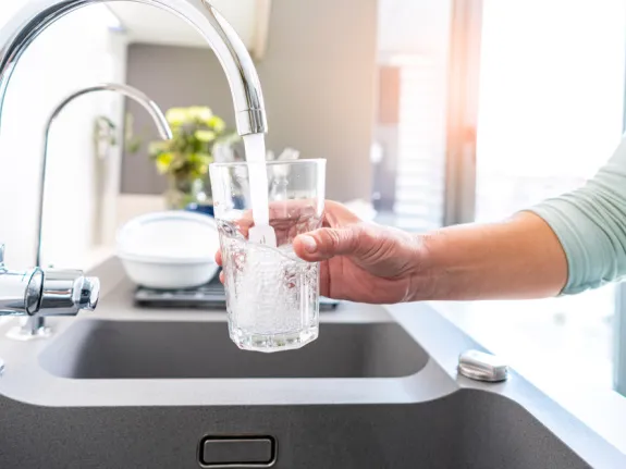 Eine Person füllt ein Glas am Wasserhahn
