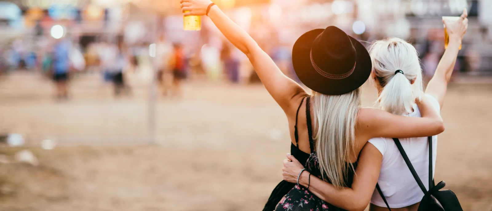 Zwei Frauen feiern am Strand. Beide halten ein Getränk in der Hand.