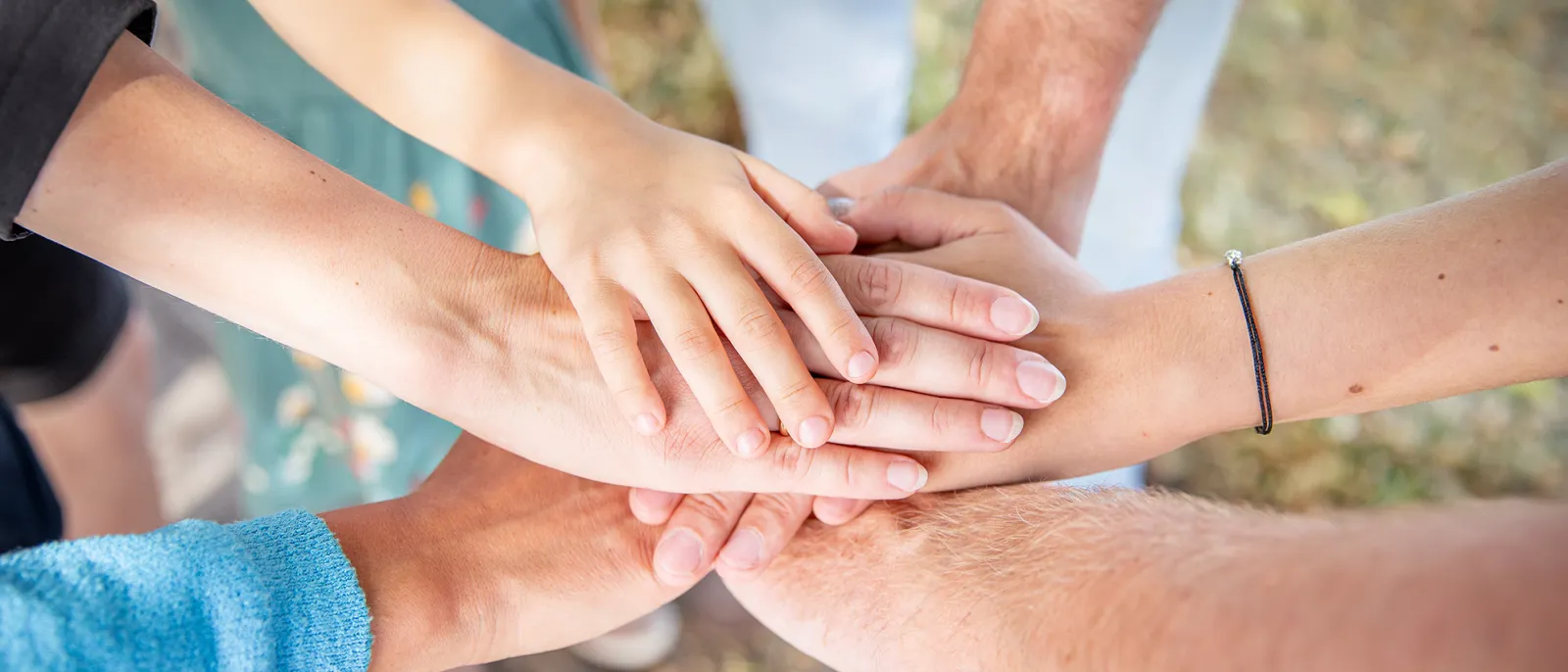 Sechs Hände von Männern, Frauen und Kindern übereinander gelegt.
