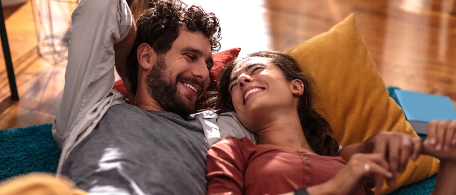 Ein junges Paar liegt gemeinsam auf dem Sofa und lächelt sich an.