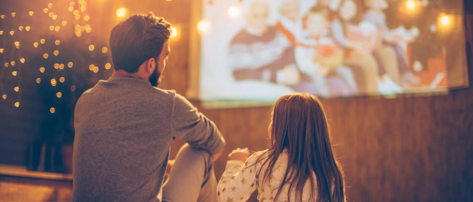 Vater und Tochter schauen zusammen einen Film im Heimkino an. Der Raum ist stimmungsvoll mit Lichterketten dekoriert.