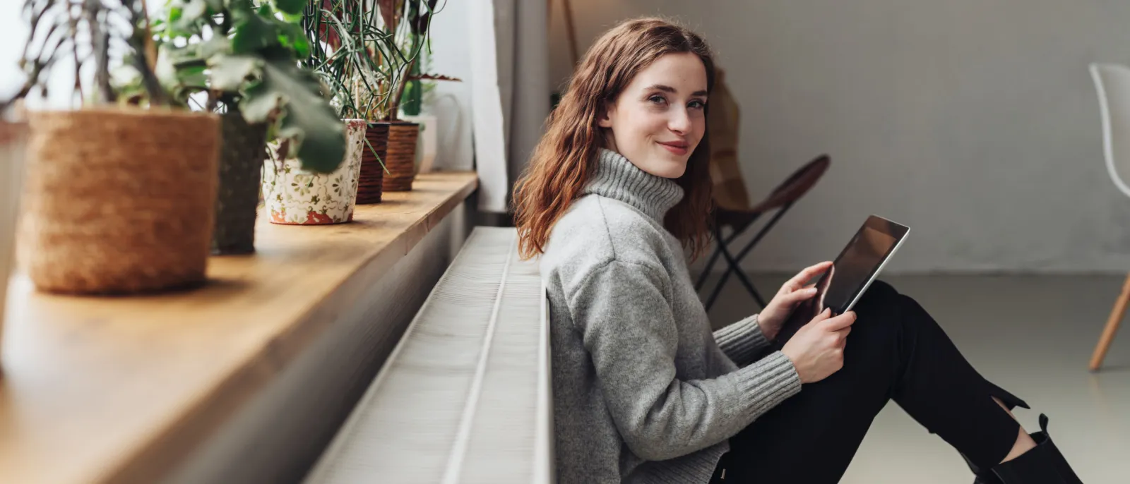 Eine Frau sitzt auf dem Boden an eine Heizung gelehnt und lächelt.