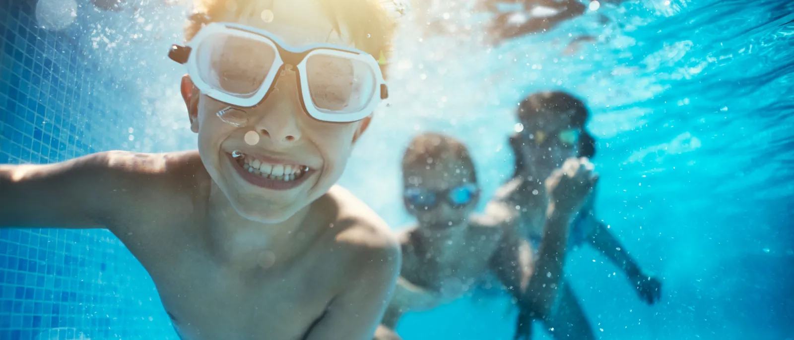 Kinder schwimmen im Pool und lächeln in die Kamera.