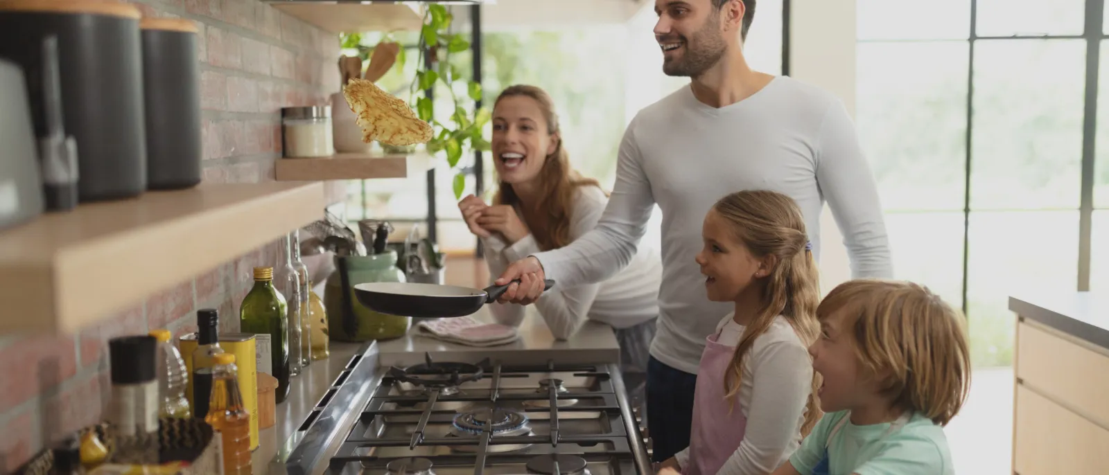 Eine Familie steht am Gasherd und macht Pfannkuchen.