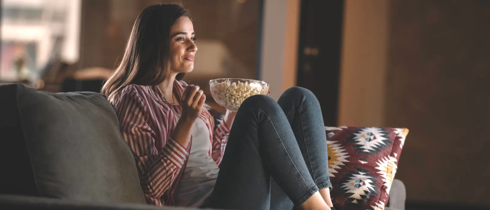Eine Frau sitzt auf dem Sofa mit Popcorn in der Hand und schaut einen Film in der Nacht.