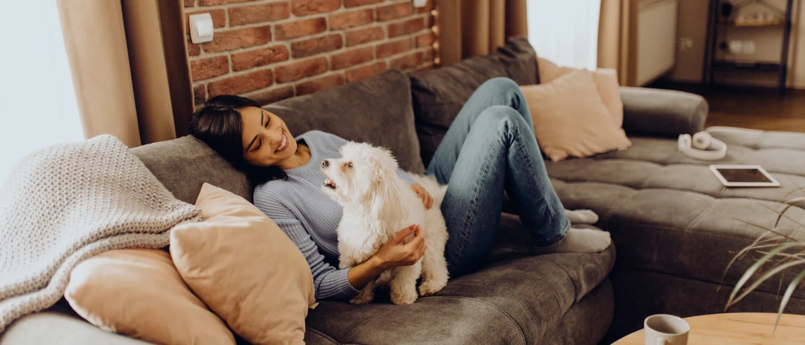 Frau liegt auf dem Sofa und streichelt ihren Hund