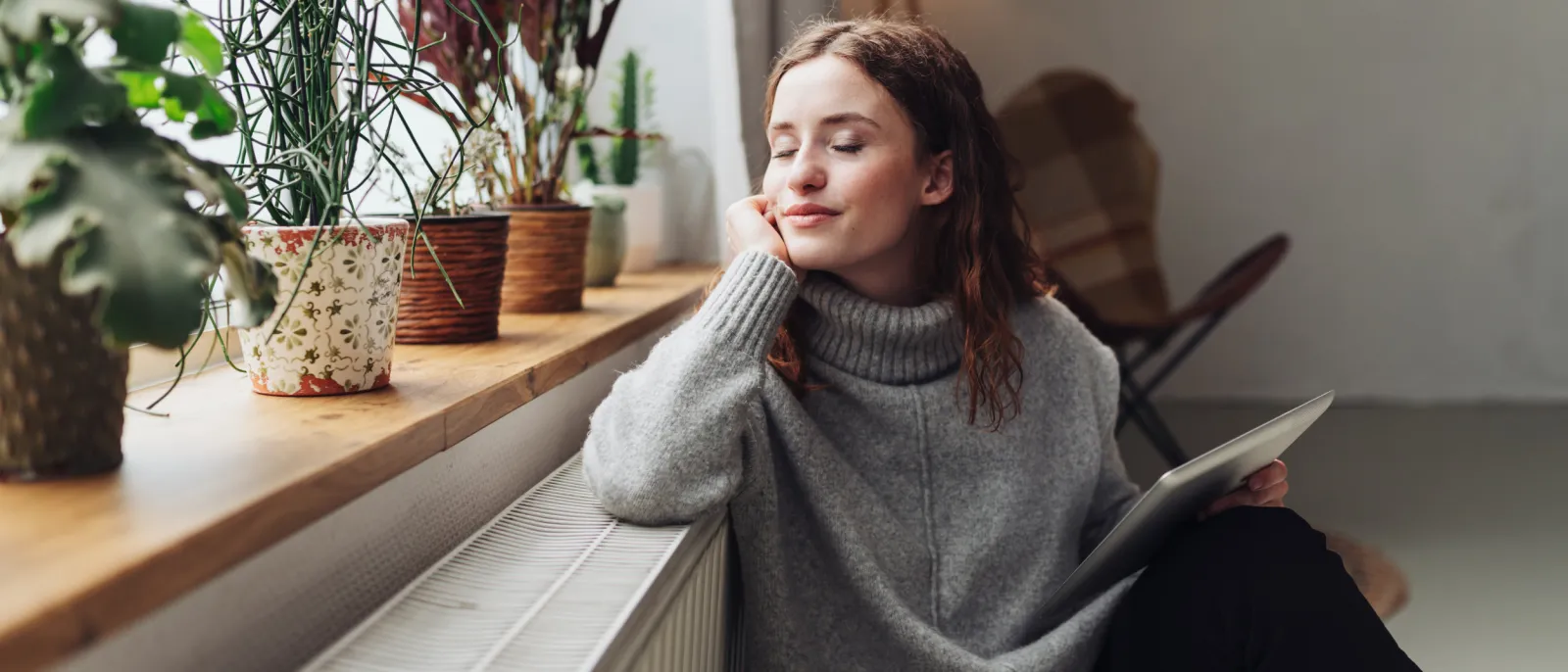 Eine junge Frau sitzt mit einem Tablet in der Hand an der Heizung und entspannt.