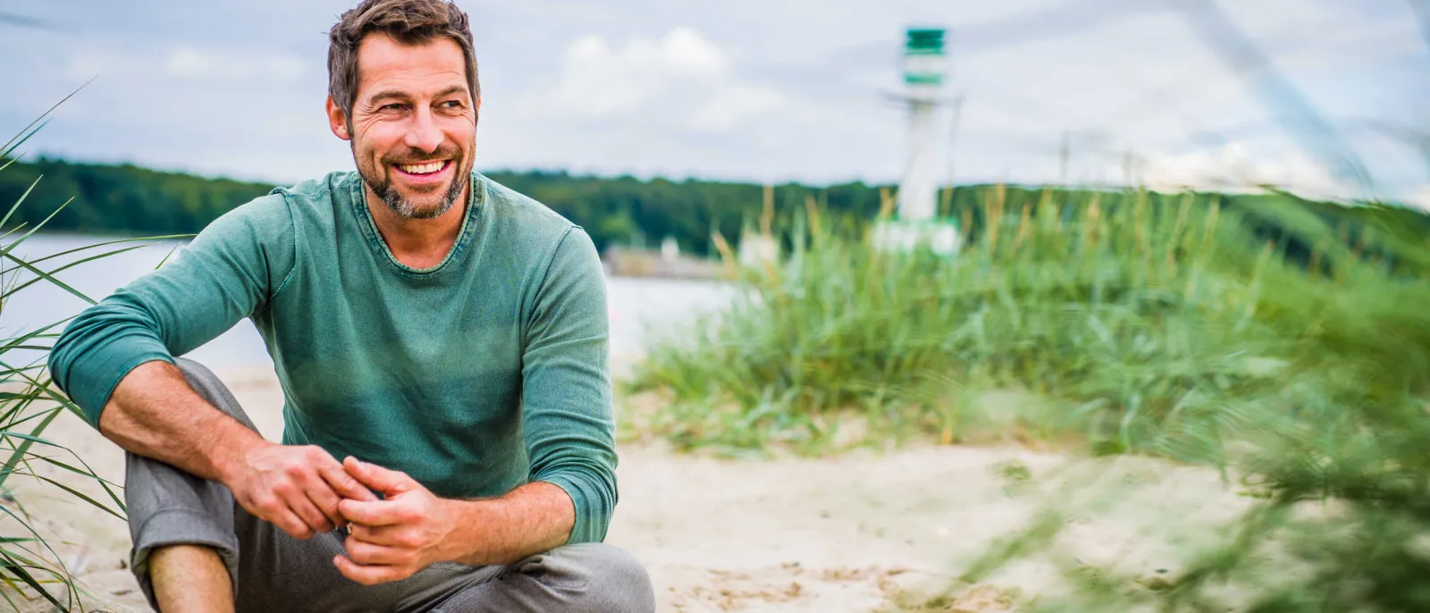 Ein Mann sitzt entspannt am Strand. Hinter ihm steht ein Leuchtturm.