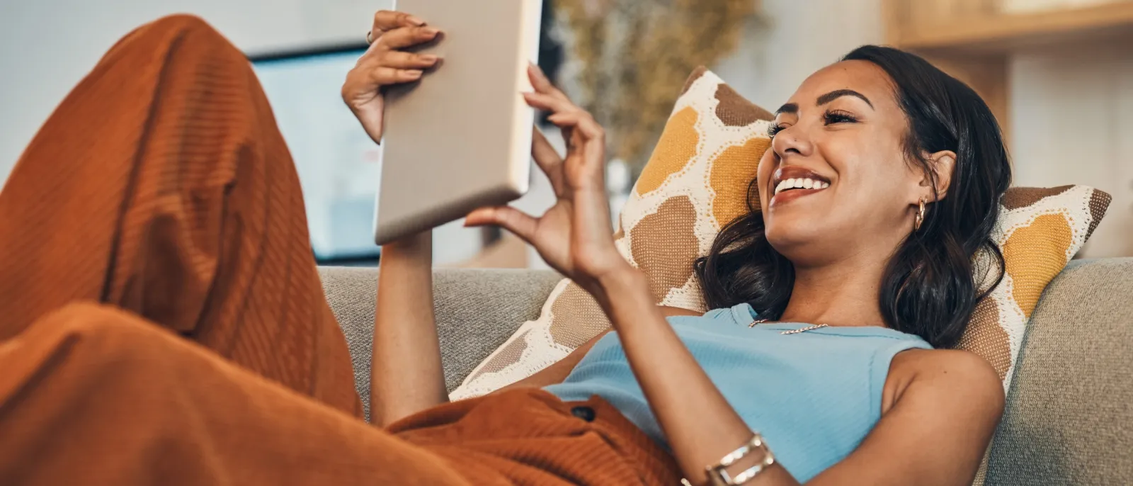 Eine Frau surft mit ihrem Tablet auf ihrem Sofa.