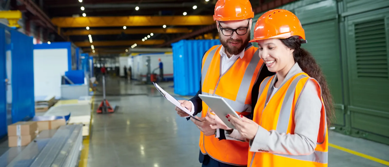Zwei Mitarbeitende stehen in einer Produktionshalle und schauen auf ein Tablet.