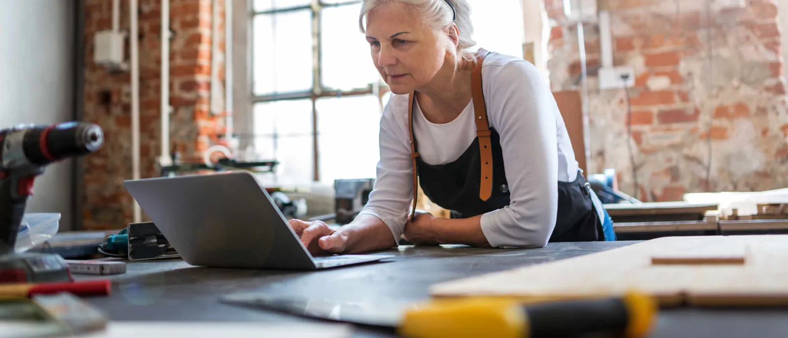Eine Frau steht an der Werkbank und schaut auf ihren Laptop.