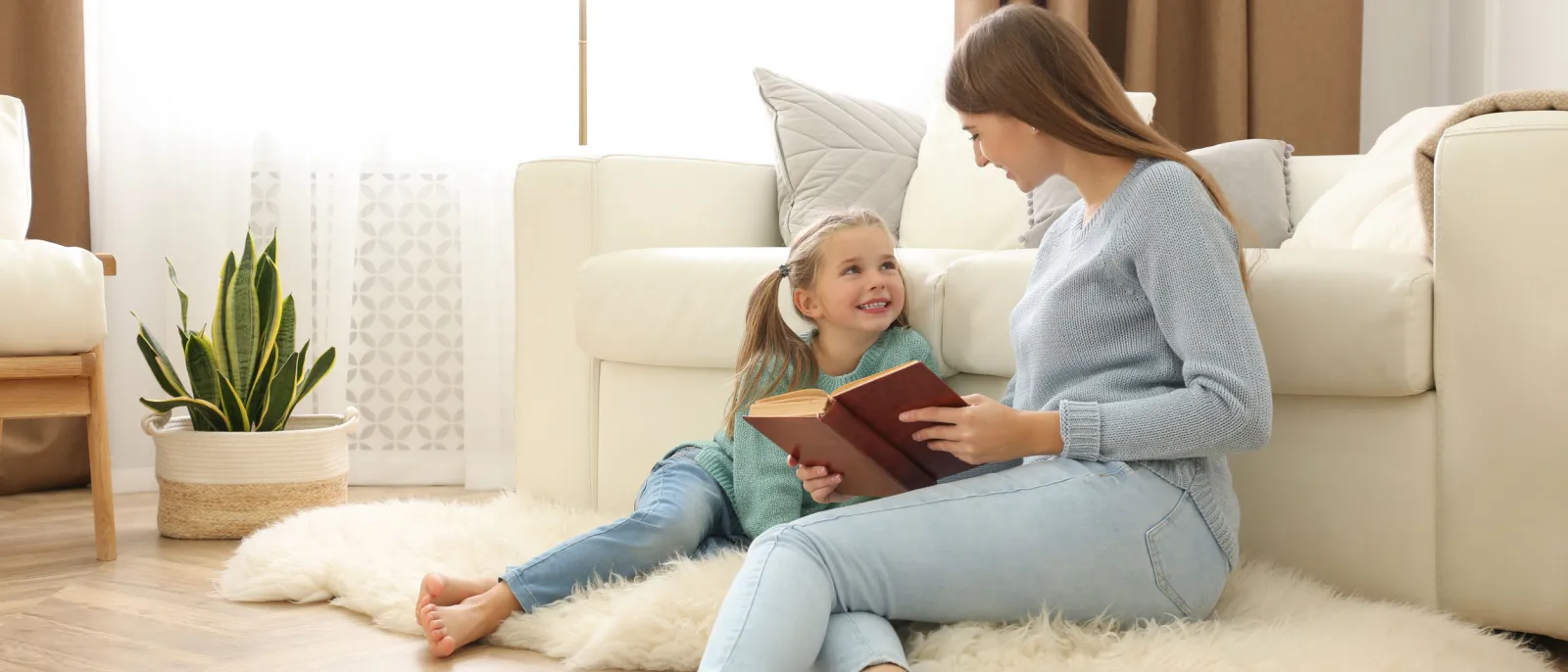 Eine Frau sitzt mit ihrer Tochter auf dem Boden und liest ihr vor.