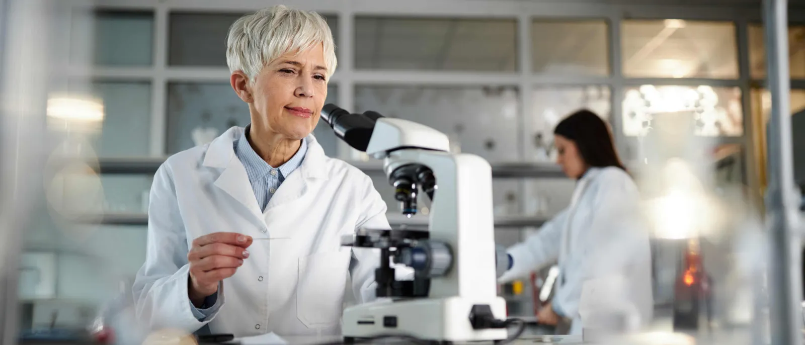 Eine ältere Wissenschaftlerin benutzt ein Mikroskop.