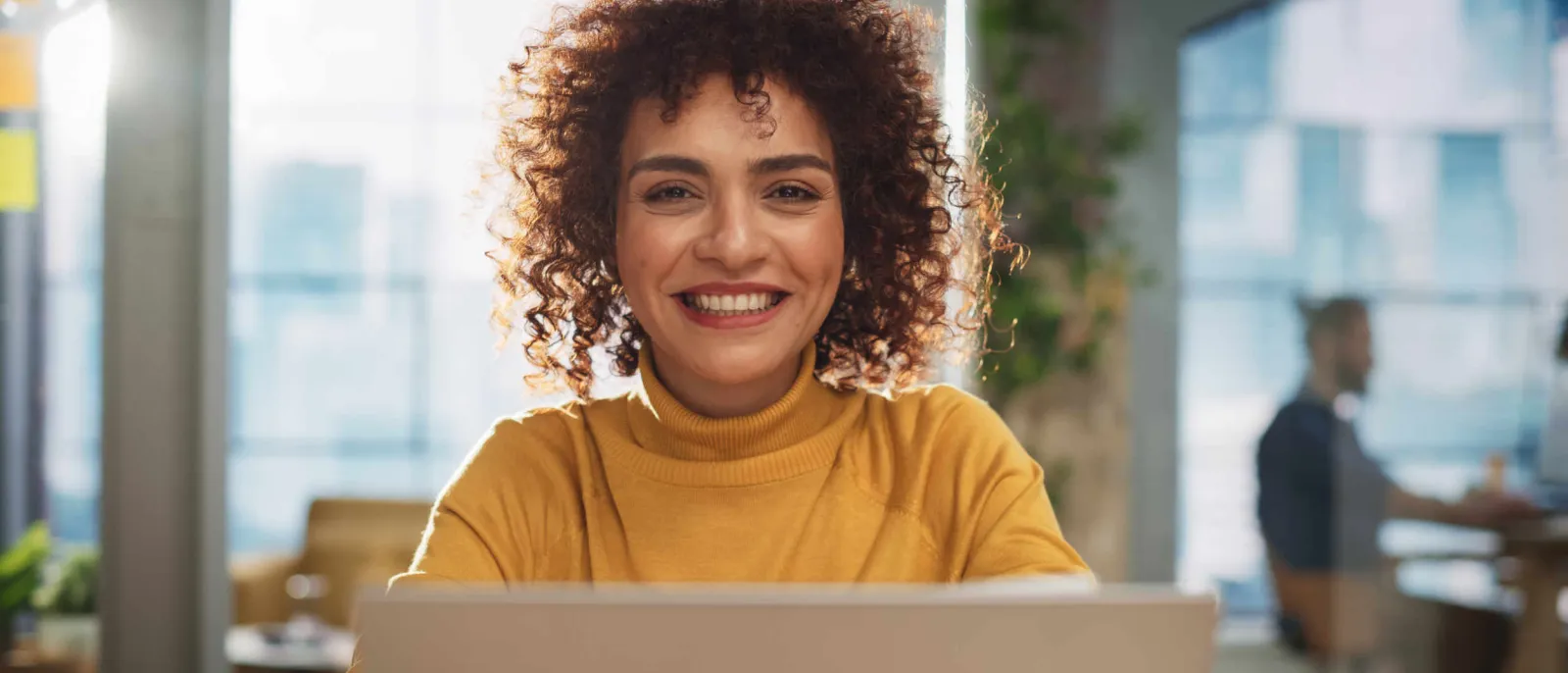 Eine Frau sitzt vor ihrem Laptop und lächelt in die Kamera.